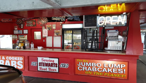 A vibrant seafood stand with a neon "OPEN" sign, featuring a menu and signs for crabs and crab cakes.