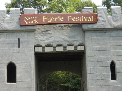 Entrance to the New York Faerie Festival, featuring a stone castle archway with a wooden sign above.