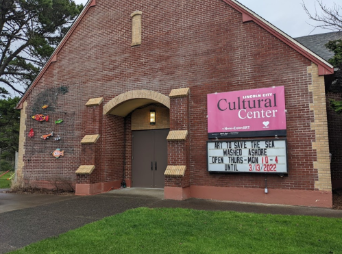 Exterior of the Lincoln City Cultural Center with a sign about an art exhibit and colorful fish decorations on the wall.