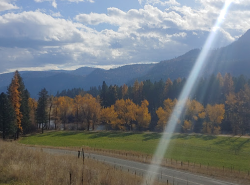 A scenic view of mountains and trees with autumn foliage, under a bright sky with clouds and sunlight streaming down.