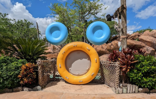 A playful arrangement of pool floats in bright colors, surrounded by tropical plants and rocky scenery.