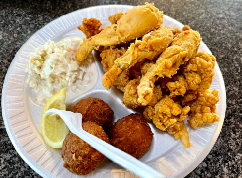 A plate of fried chicken pieces, coleslaw, and two hushpuppies, garnished with lemon wedges.