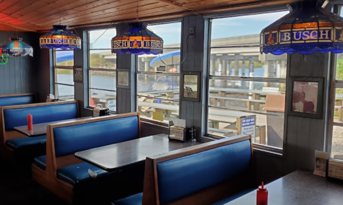 Interior of a cozy diner with blue booths, stained glass lamps, and a view of a waterfront pier through large windows.