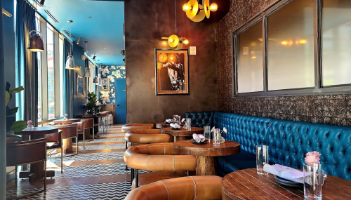 Stylish restaurant interior with blue walls, leather seating, and decorative lighting, featuring floral accents and wooden tables.