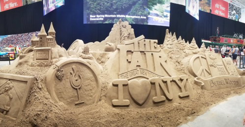 A large sand sculpture featuring landmarks and symbols from New York, with the text "The Fair" and "I ❤️ NY."