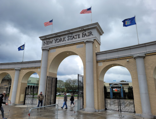 Entrance to the New York State Fair, featuring flags and a cloudy sky.