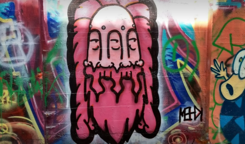 A colorful graffiti mural featuring a pink, bearded figure with multiple eyes and abstract designs in the background.