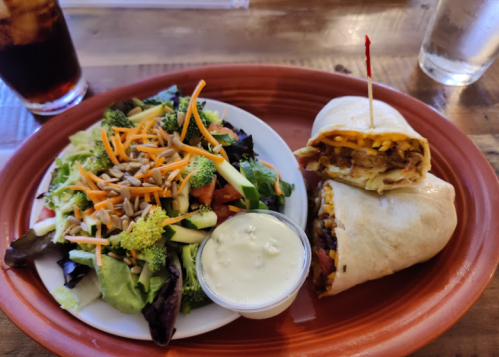 A plate with a wrapped burrito and a side salad topped with broccoli, carrots, and a creamy dressing.