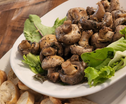 A plate of sautéed mushrooms garnished with lettuce, served alongside slices of toasted bread.
