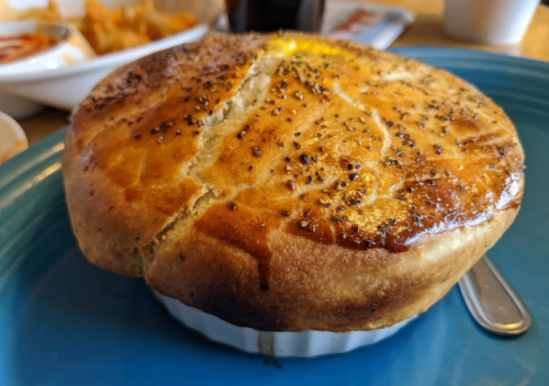 A golden-brown pot pie with a flaky crust, resting on a blue plate, with a spoon beside it.