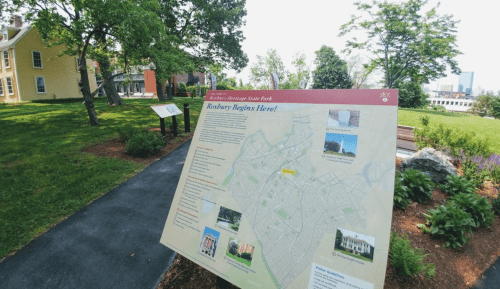 A map sign in a park, showing the layout of the area with trees and buildings in the background.