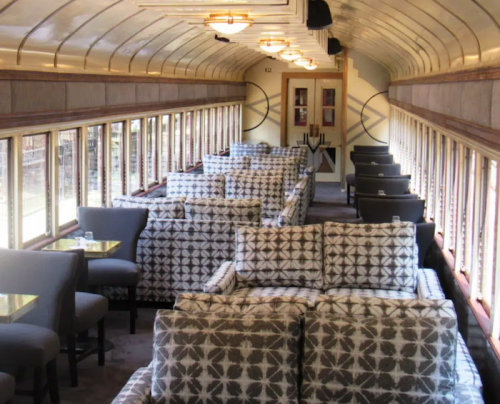 Interior of a vintage train car featuring plush, patterned seating and large windows, creating a cozy atmosphere.
