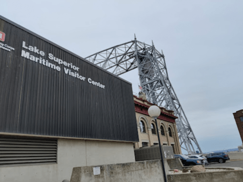 A building with a sign for the Lake Superior Maritime Visitor Center, with a large metal structure in the background.