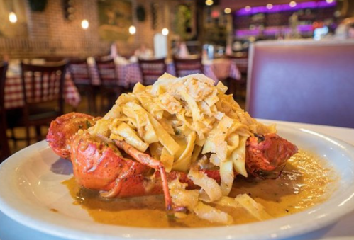 A plate of lobster topped with fettuccine in a creamy sauce, set in a cozy restaurant with checkered tablecloths.