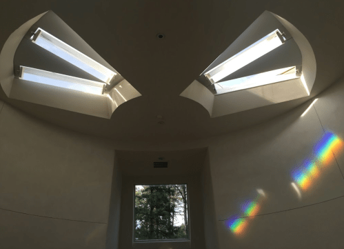 Interior view of a room with two skylights and a rainbow reflection on the wall. Natural light fills the space.