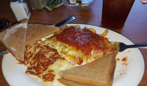 A plate with a cheesy omelet topped with salsa, hash browns, and two slices of toast, alongside a glass of iced tea.