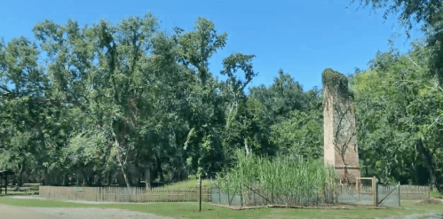 A tall, weathered stone structure surrounded by lush greenery and trees under a clear blue sky.