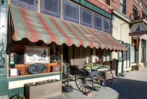 Exterior of The Virginian restaurant featuring a striped awning, vintage carriage, and flower planters.