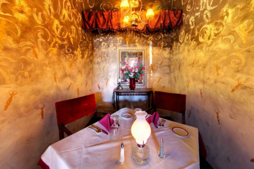 Cozy restaurant corner with ornate walls, a floral centerpiece, and a vintage lamp on a white tablecloth.