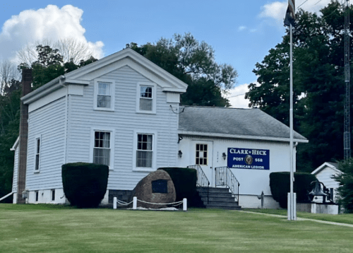 A white building with a sign for Clark-Bick Post 568 American Legion, surrounded by green grass and trees.