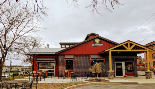 A red and brick building with a sign, outdoor seating, and bare trees, set against a cloudy sky.