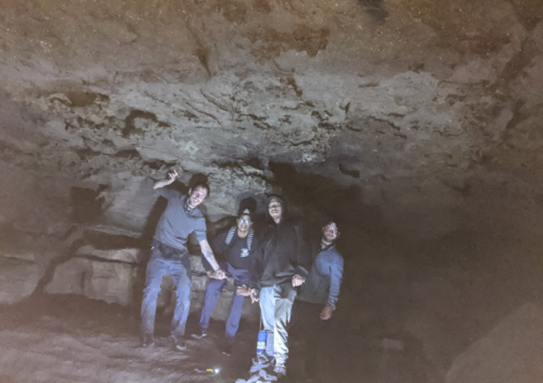 Four people pose in a dimly lit cave, smiling and standing under a rocky ceiling.