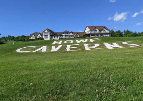 A grassy hillside with large white letters spelling "HOWF CAVERNS" in front of a building under a clear blue sky.