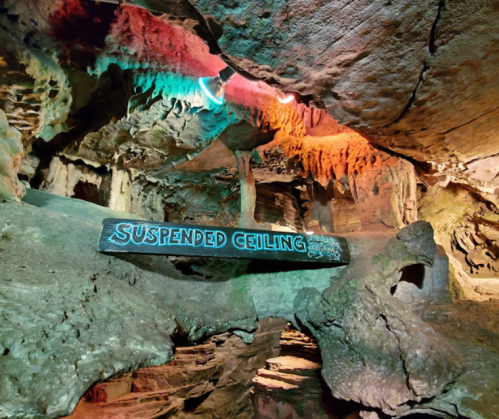 A colorful cave interior featuring a sign that reads "SUSPENDED CEILING" amidst rock formations and lighting.