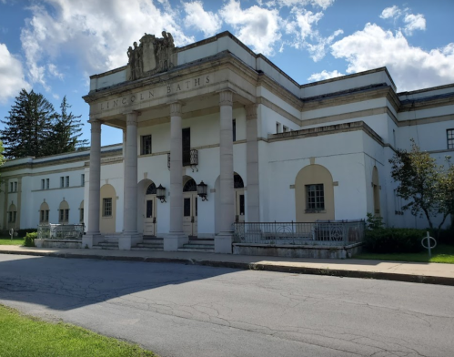 Historic building with a grand entrance, featuring columns and a sign that reads "Lincoln Baths," set against a blue sky.