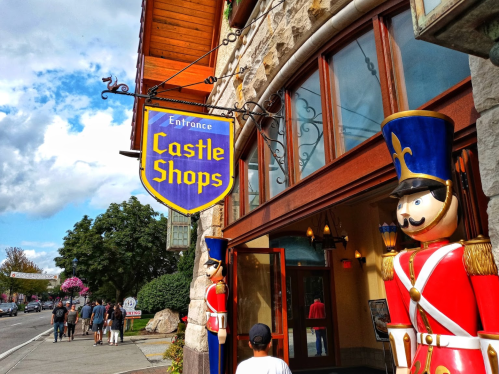 Entrance to Castle Shops with colorful sign and toy soldier decorations, surrounded by trees and people walking by.