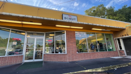 Exterior of The Donut Shoppe, featuring large windows, an "OPEN" sign, and a bright yellow awning.