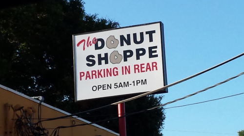 Sign for "The Donut Shoppe" with parking instructions, open from 5 AM to 1 PM.