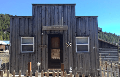 A rustic wooden building with a sign reading "Lemon Trading Post," surrounded by a picket fence and blue sky.