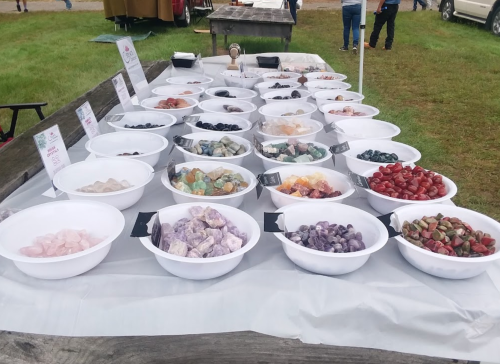 A display of colorful candies in white bowls on a table, set up outdoors at a market.