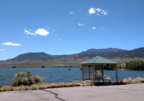 A gazebo by a lake with mountains in the background under a clear blue sky.