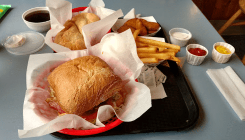 A tray with two sandwiches, fries, and potato wedges, accompanied by small cups of ketchup, mustard, and ranch dressing.