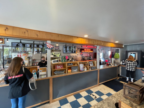 A cozy diner interior with a counter, menu boards, and customers ordering food. Red, white, and blue decor is visible.