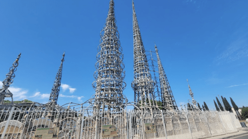 A group of tall, intricate metal towers against a clear blue sky, surrounded by a fence.