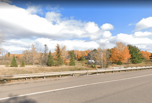 A scenic view of a highway with trees displaying autumn colors under a partly cloudy sky.