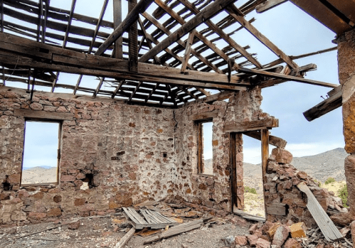 Interior of a dilapidated stone building with a partially collapsed roof and exposed wooden beams.
