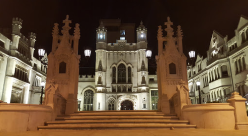 Illuminated historic building at night, featuring ornate architecture and grand stairway with decorative gates.