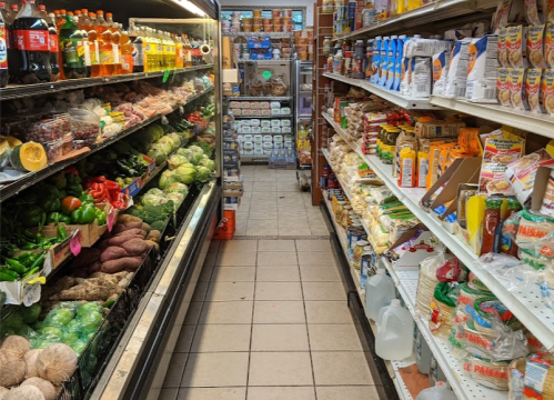 A grocery store aisle with fresh produce on one side and packaged goods on the other, creating a narrow walkway.