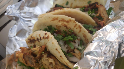 Three tacos filled with meat, onions, and cilantro, wrapped in foil.