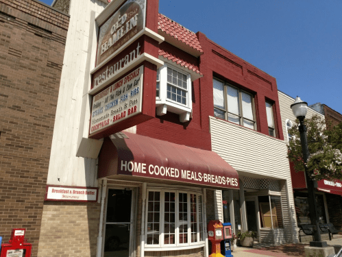 Exterior of a restaurant with a red awning, sign displaying "Home Cooked Meals, Breads, Pies," and a salad bar.