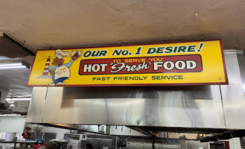 A colorful sign in a restaurant kitchen reads "Our No. 1 Desire! To Serve You Hot Fresh Food - Fast Friendly Service."
