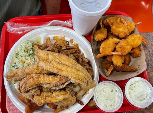 A tray with fried fish, shrimp, coleslaw, and two cups of dipping sauce.