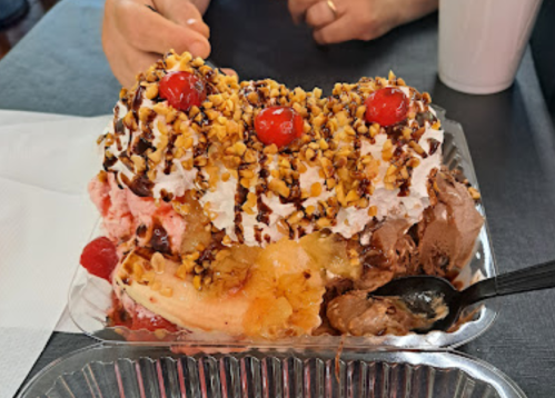 A colorful ice cream sundae topped with whipped cream, cherries, nuts, and chocolate sauce in a plastic dish.