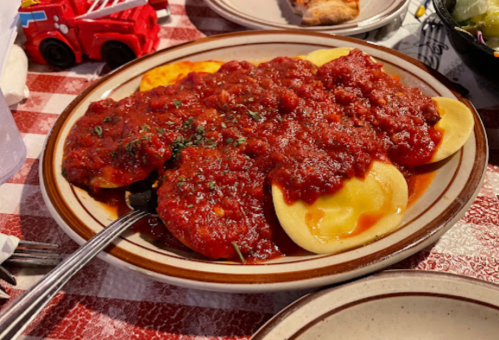 A plate of ravioli topped with a rich red sauce and sprinkled with herbs, served on a checkered tablecloth.