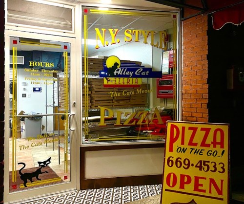 A pizzeria storefront with a sign reading "N.Y. Style Alley Cat Pizzeria" and a bright "OPEN" sign.