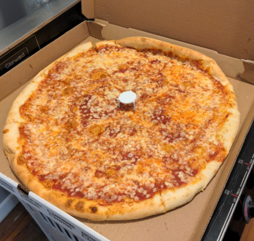 A large cheese pizza in a cardboard box, featuring a golden crust and a small white pizza saver in the center.